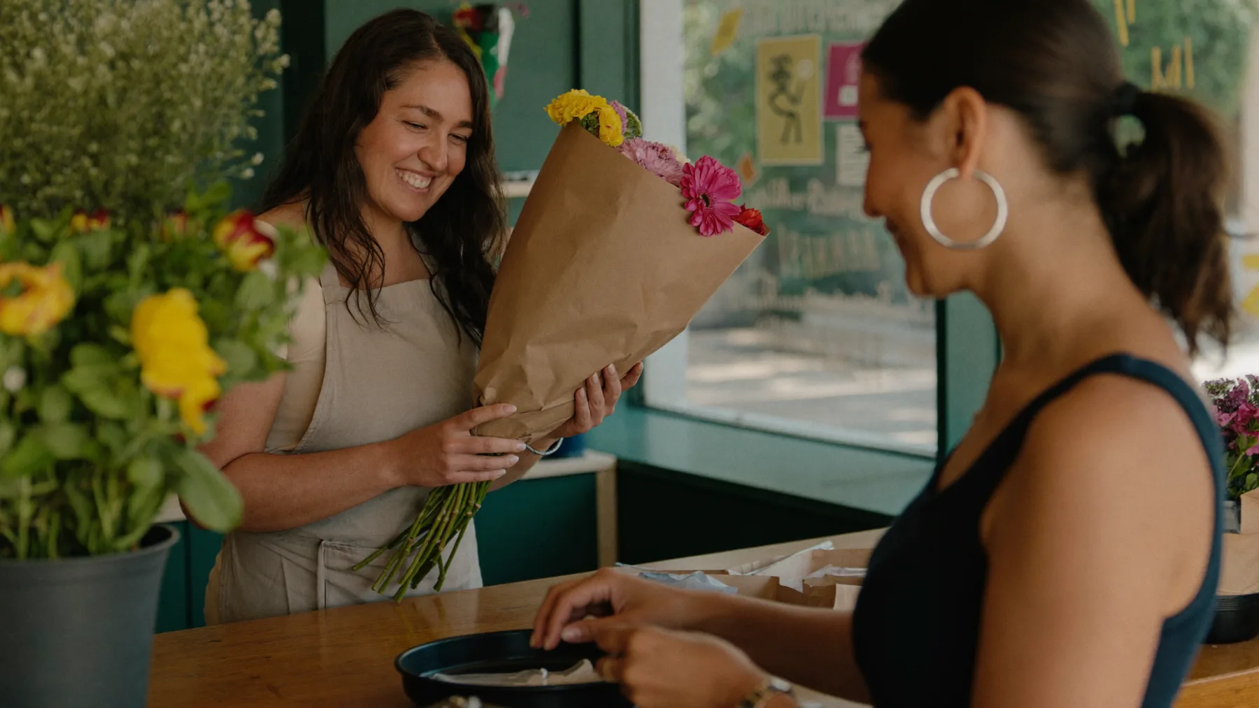 Una florista entrega un ramo recién envuelto a su clienta en el mostrador de la tienda.