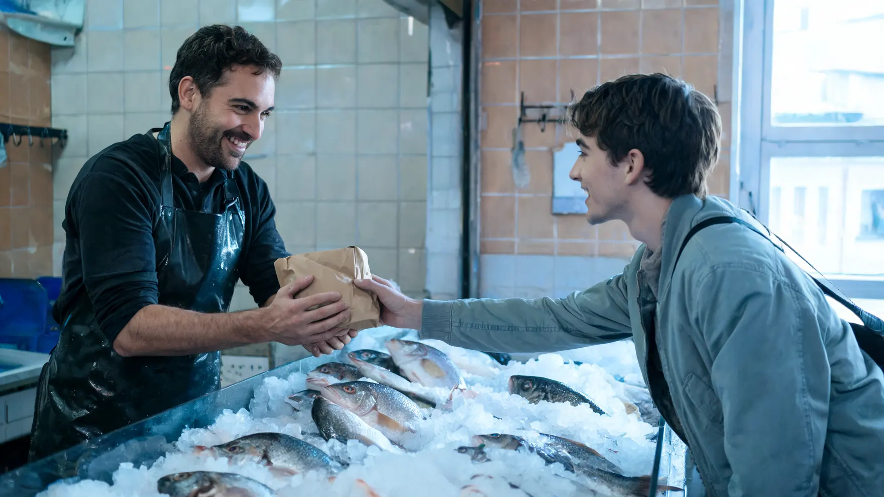 Un pescadero entrega la bolsa con el pescado a un cliente por encima del hielo.